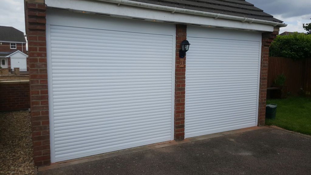 Pair of white electric roller garage doors on a double garage with brick pillars in Tetbury