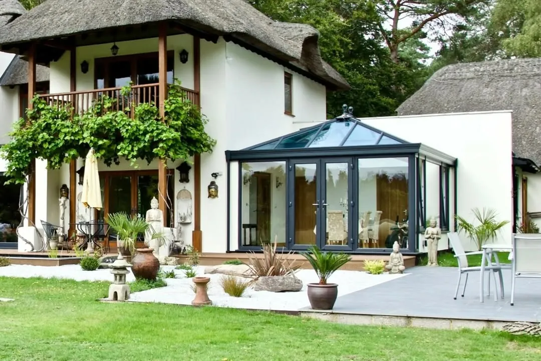 Anthracite grey glass conservatory roof on a white thatched house with a landscaped garden, Meysey Hampton