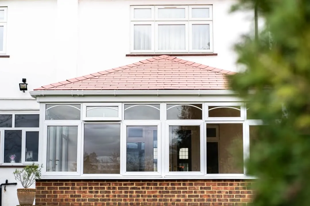 Terracotta tiled conservatory roof on a white rendered house with white glazing below, Newbury