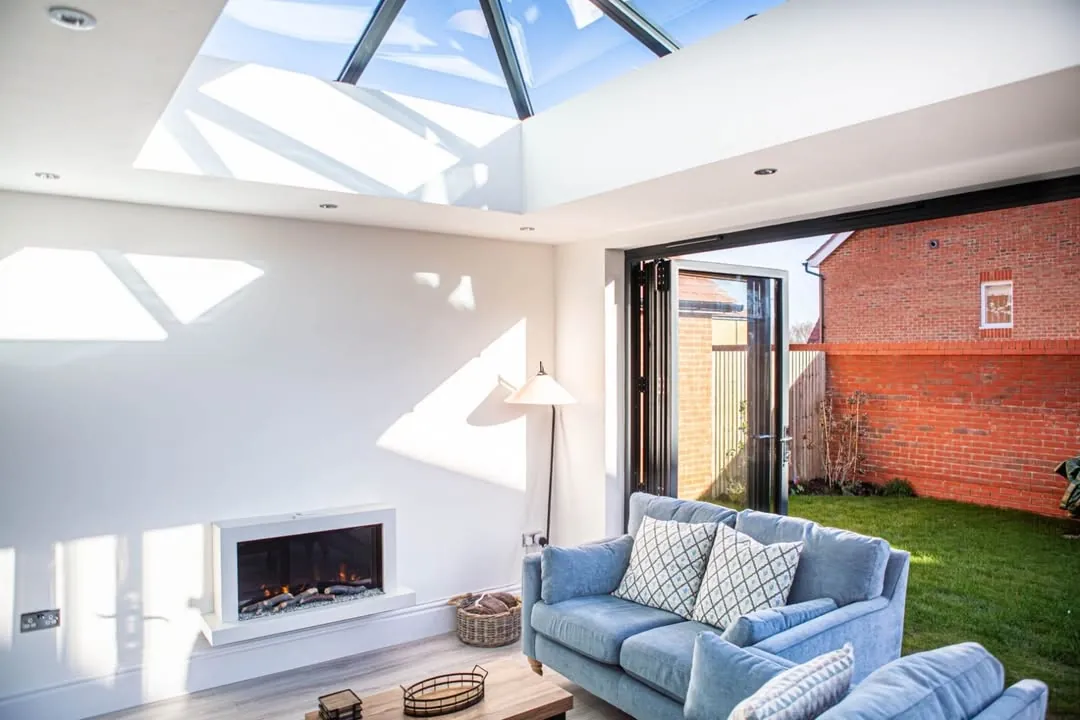 Living space under a white glazed roof lantern with bifold doors open to a garden, Highworth