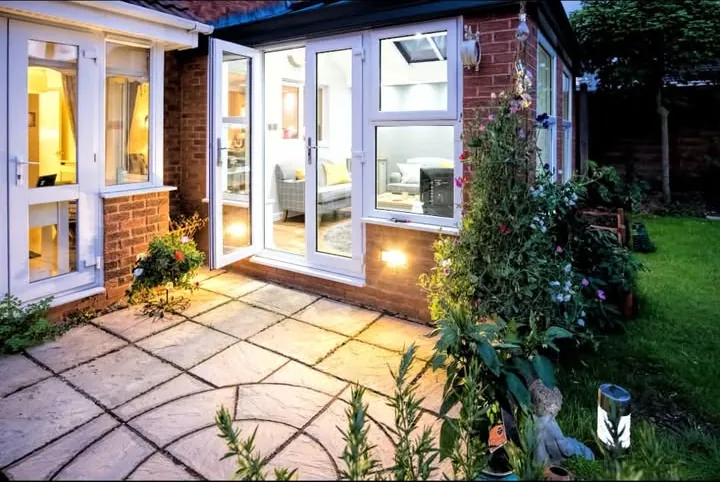 Conservatory lit from inside at dusk with white French doors open onto a paved patio, Sandford-on-Thames