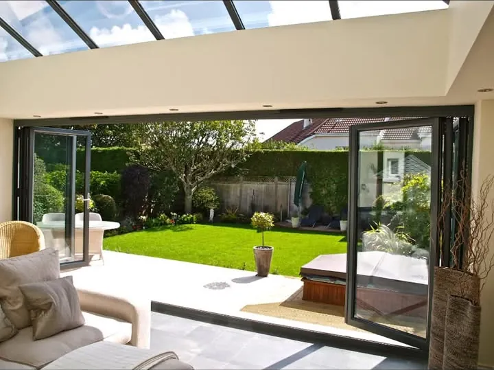 Anthracite grey aluminium bifold doors folded open from a garden room onto a lawn, South Cerney
