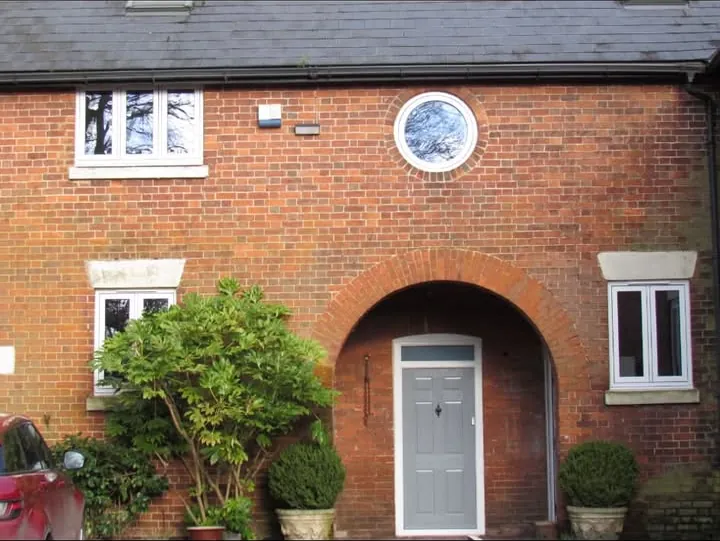 Grey panelled composite front door set in an arched brick porch with white windows either side, Henley-on-Thames