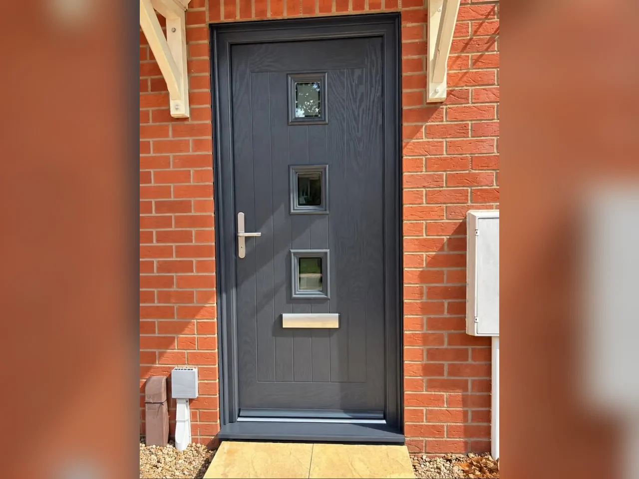 Anthracite grey cottage-style composite front door with three square glazed panels in a red brick porch, Trowbridge