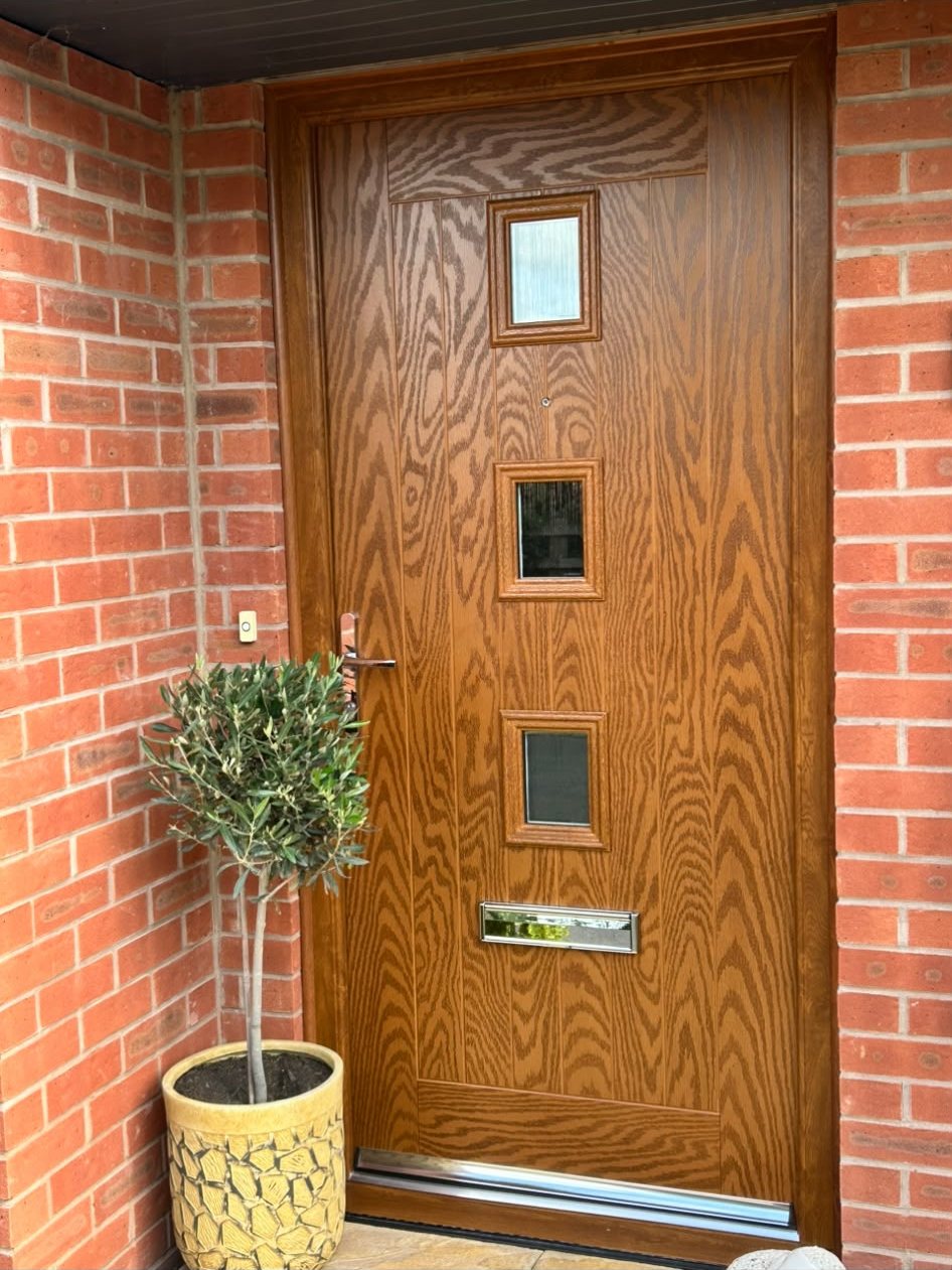 Golden oak woodgrain composite front door with three square glazed apertures in Innsworth, Gloucestershire