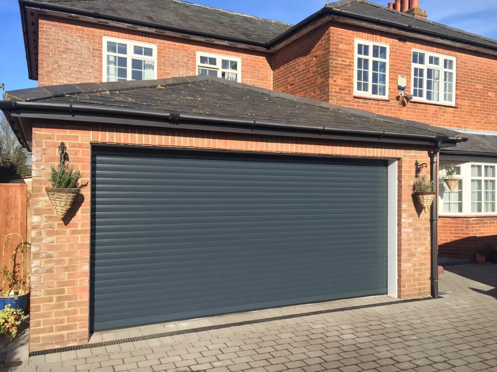 Wide anthracite insulated roller door on a brick double garage beside a detached house