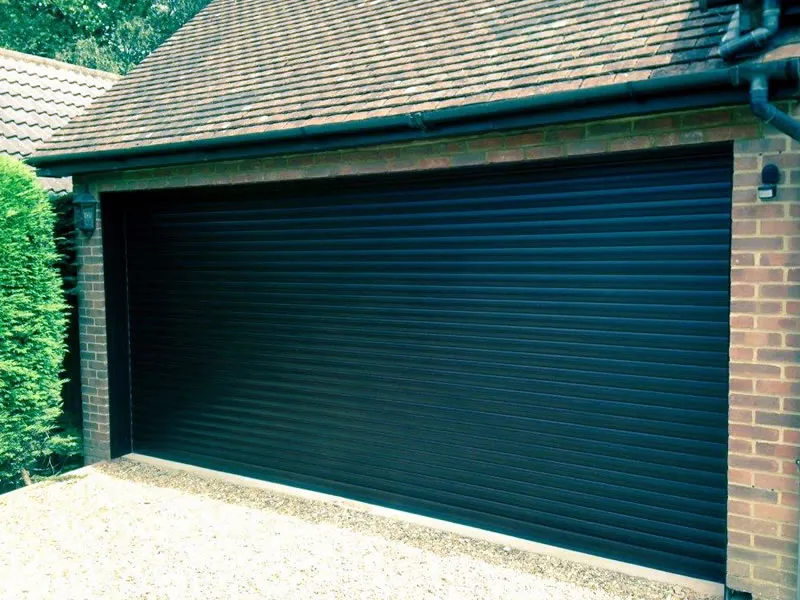 Black insulated roller door on a brick double garage with a gravel drive
