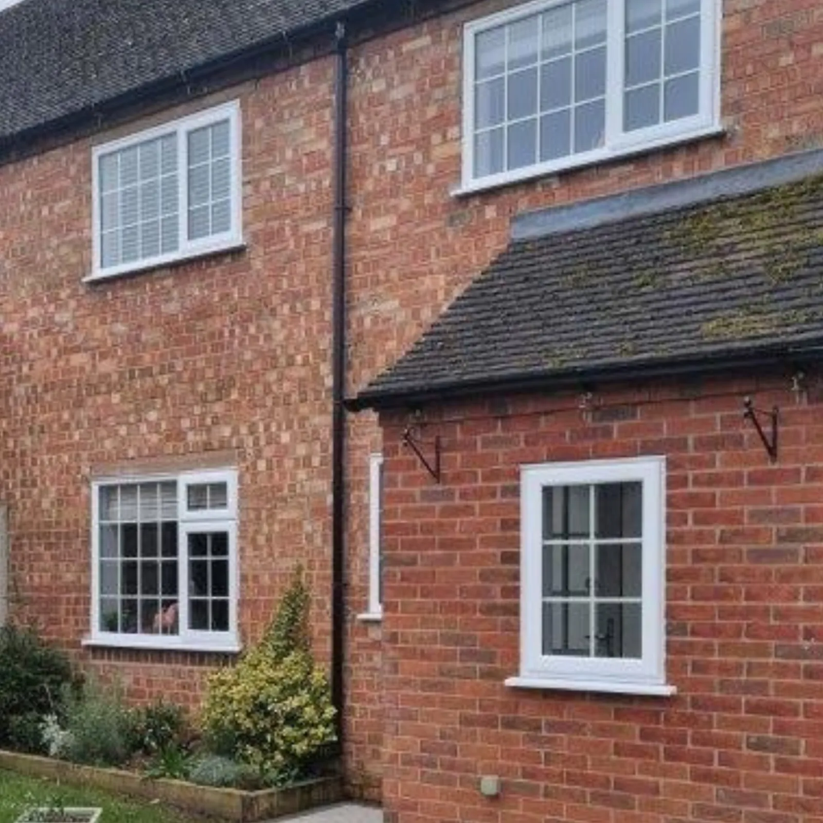 White casement windows with Georgian glazing bars across a red brick period house