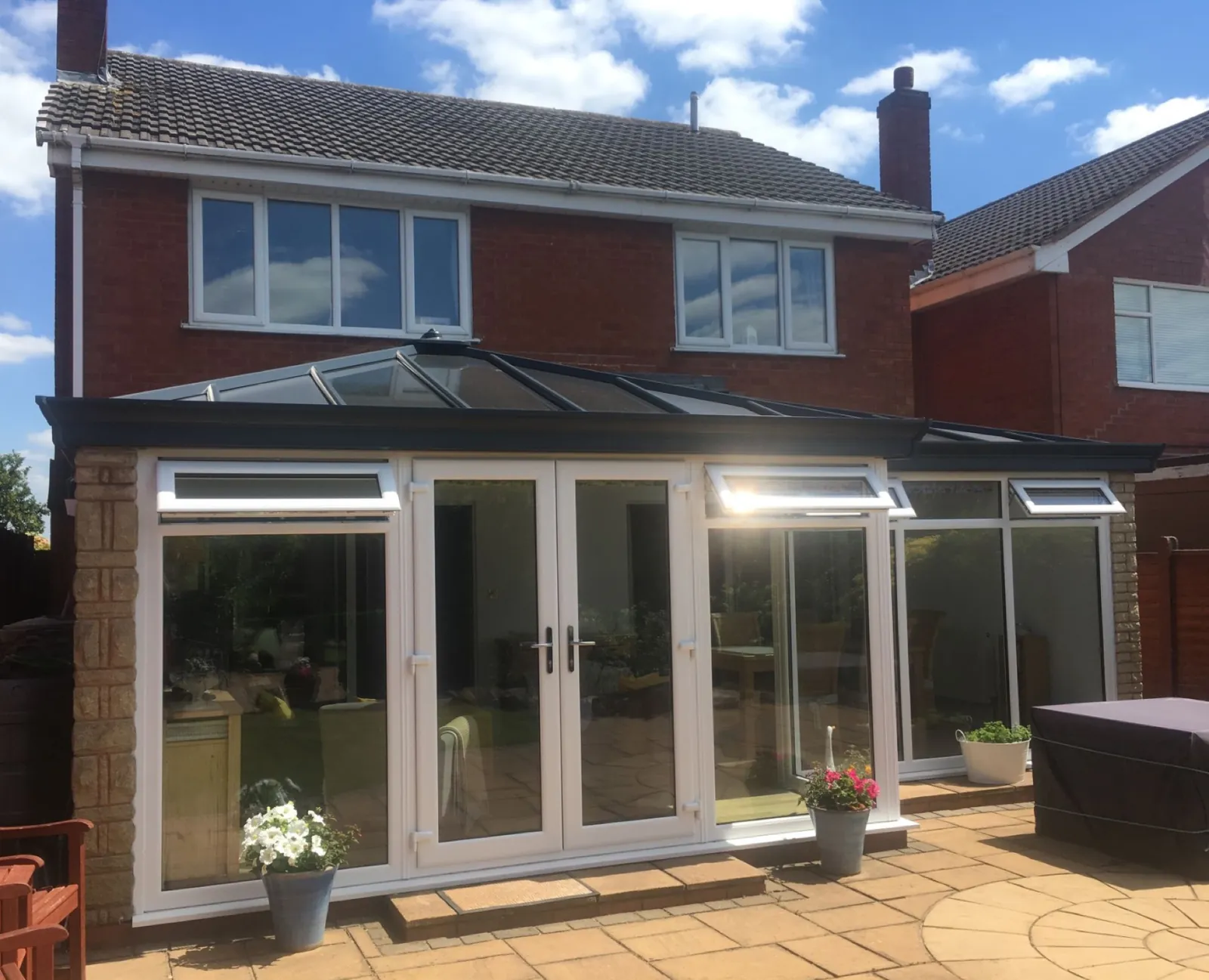 Anthracite grey glazed conservatory roof above white French doors and glazing on a red brick house