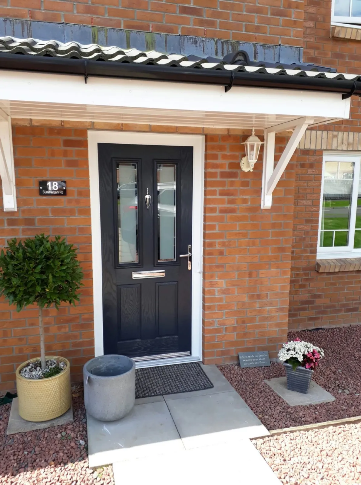 Anthracite grey composite front door with two glazed panels and a chrome letterplate in a red brick porch