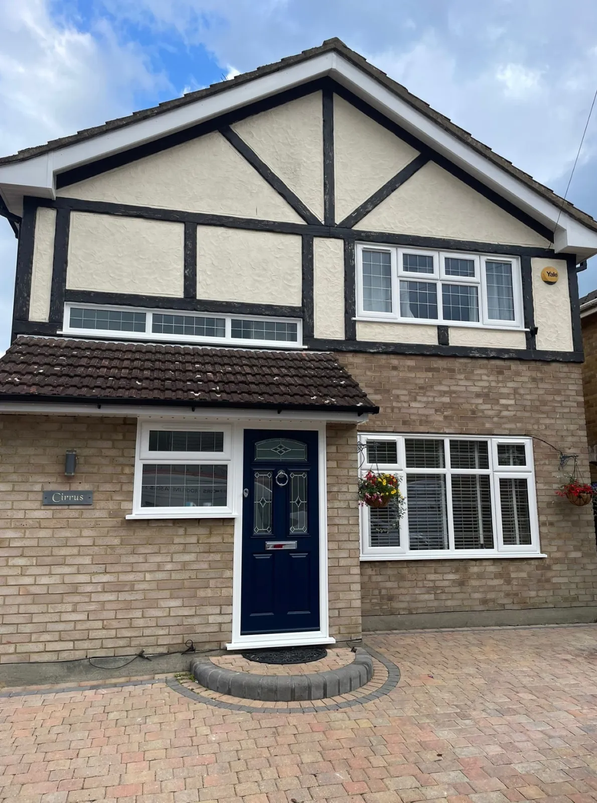 White casement and bay windows with leaded glazing beside a navy composite front door on a mock-Tudor house
