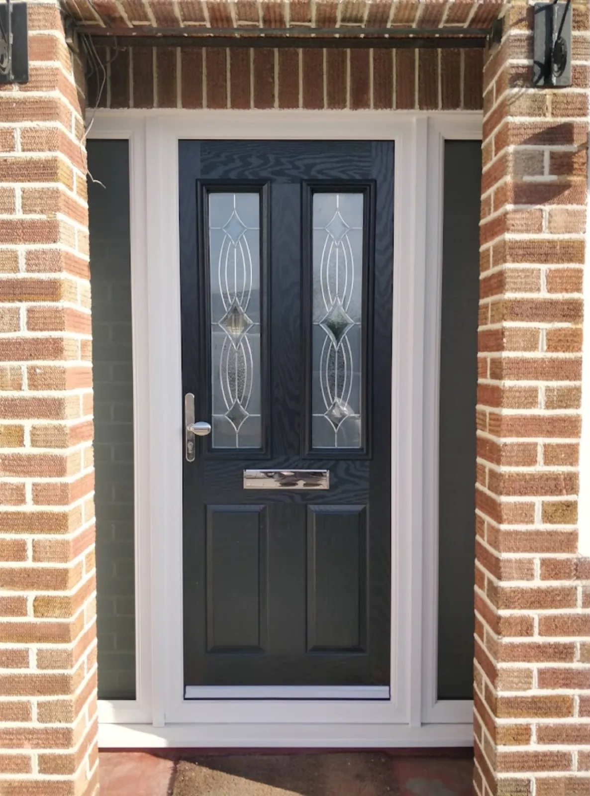 Anthracite grey composite front door with leaded glazing and slim glazed side panels between brick piers