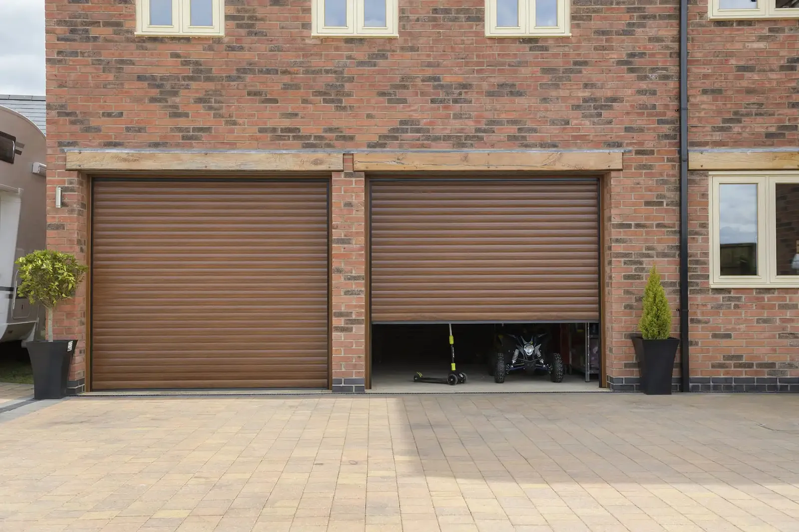 Pair of Golden Oak woodgrain roller garage doors, one partly open, on a brick double garage