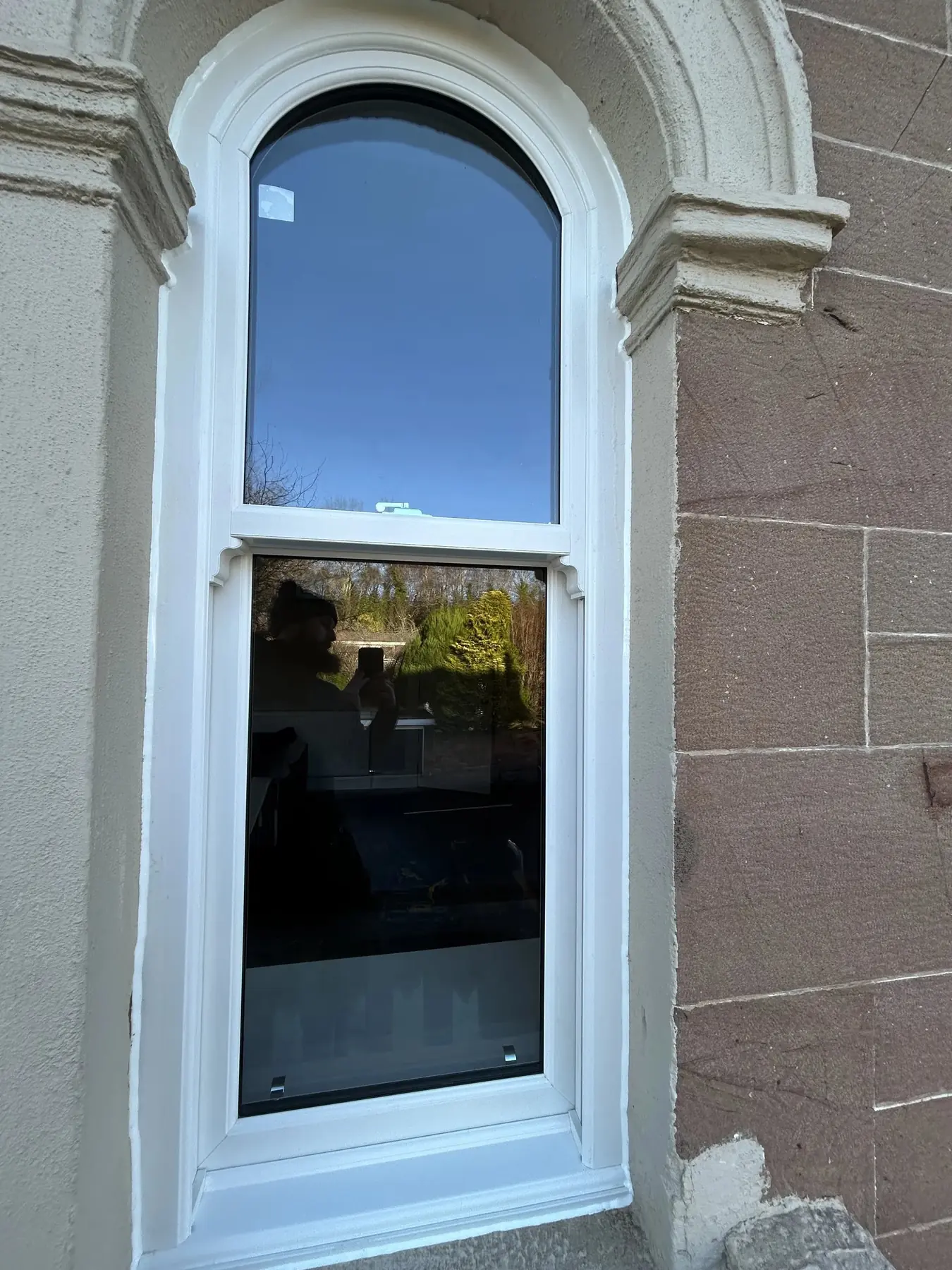 Round-headed white sliding sash window set into a stone surround