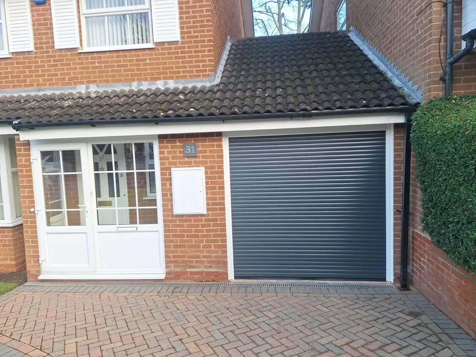 Anthracite grey insulated roller door on a link-attached single garage with a block-paved drive