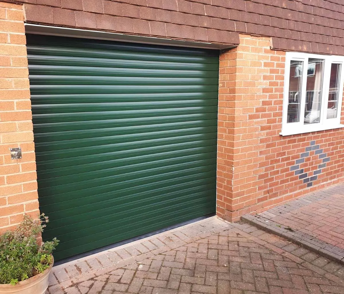 Green insulated roller garage door fitted to a brick single garage