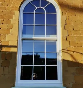 Round-headed sliding sash window with Georgian bars in a stone reveal