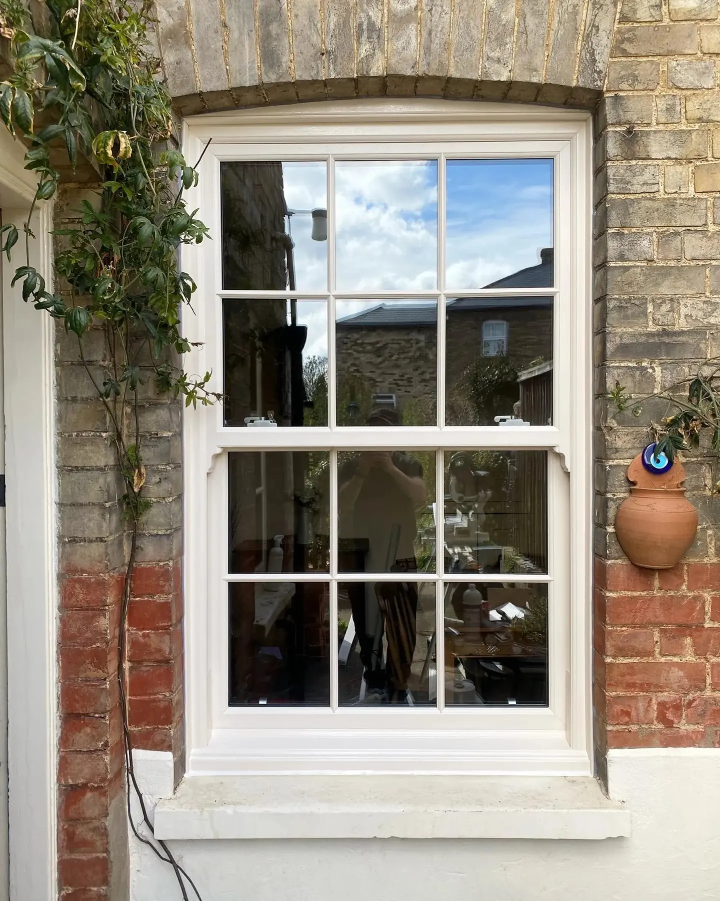 Tall white Georgian-barred sash window framed by climbing plants