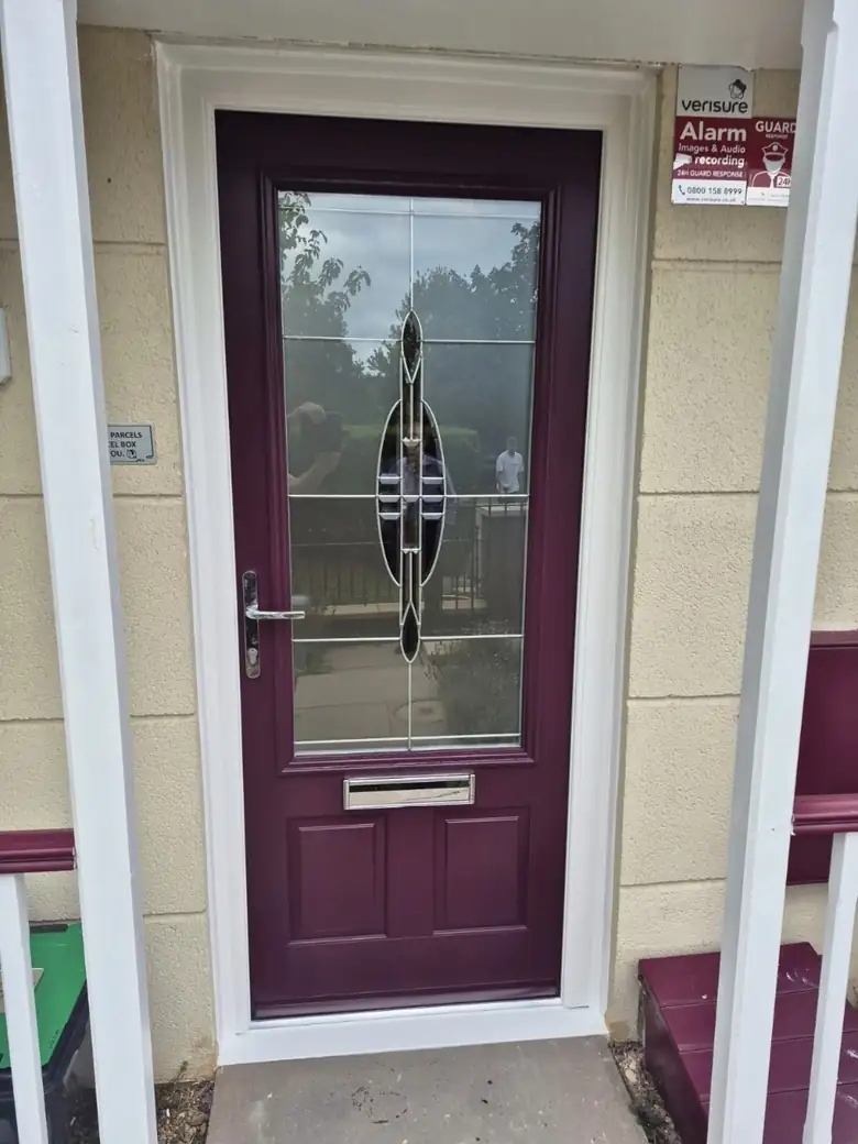 Burgundy composite front door with a decorative leaded glass panel, chrome lever handle and letterplate, and a white frame on a cream rendered home, Cheltenham