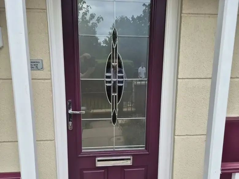 Burgundy composite front door with a decorative leaded glass panel, chrome lever handle and letterplate, and a white frame on a cream rendered home, Cheltenham