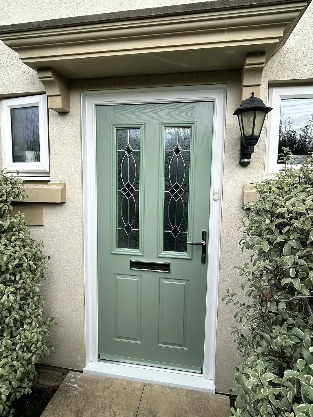 Chartwell Green composite front door with tall leaded glass panels, chrome letterplate and white frame beneath a stone canopy, Melksham