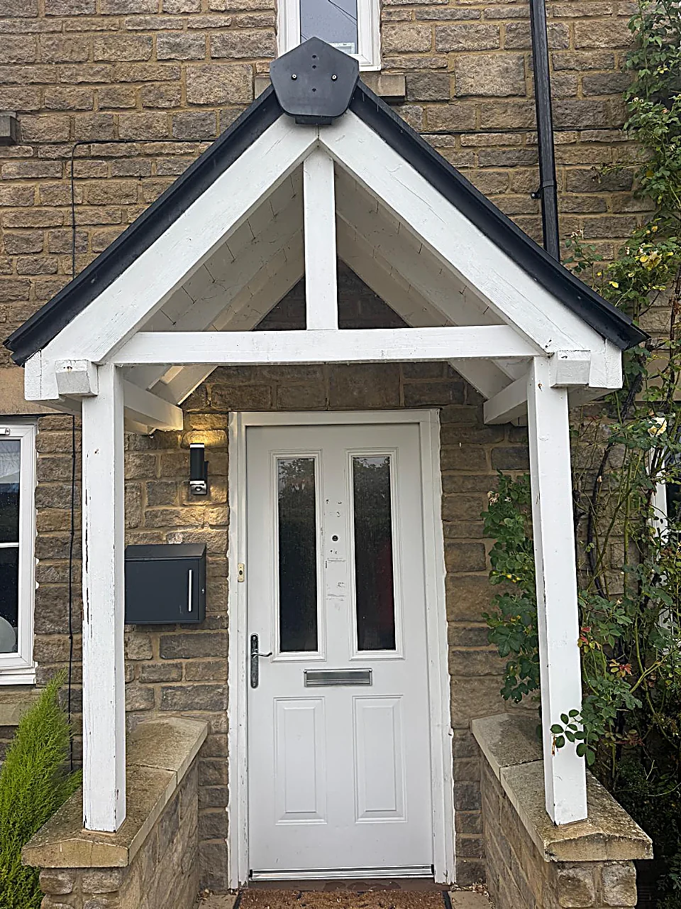 The old white four-panel front door before replacement, with two glazed panels, chrome letterplate and marked paintwork, beneath a white timber porch, Cricklade