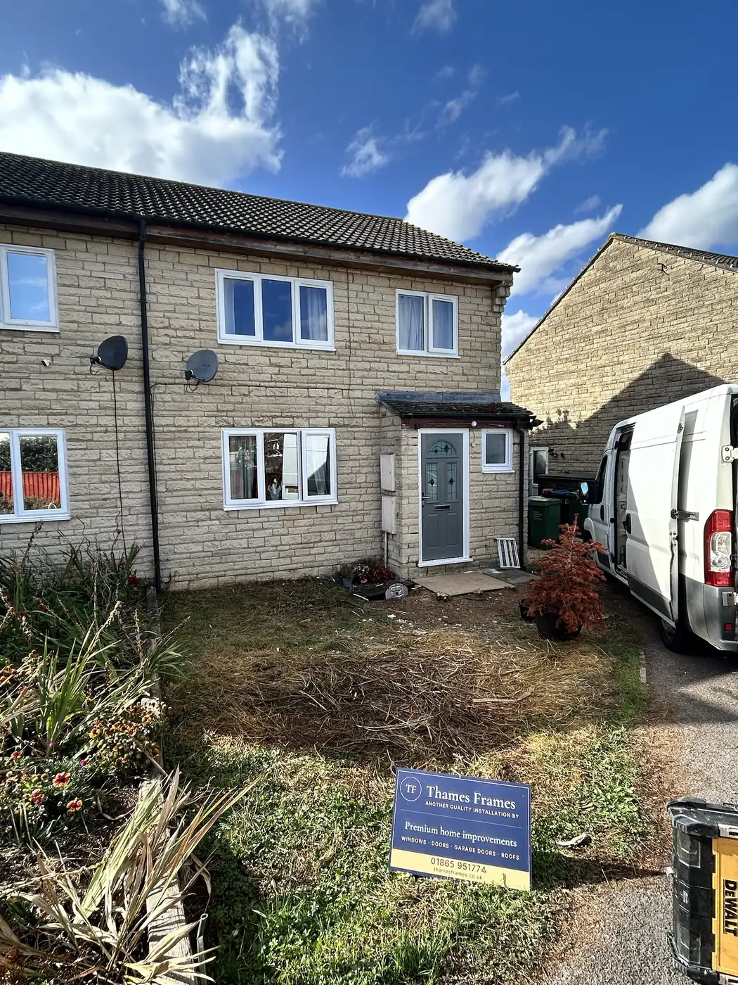 Front of a renovated semi-detached house in Cricklade with new white windows, a Shadow Grey composite door and a Thames Frames installation board on the lawn
