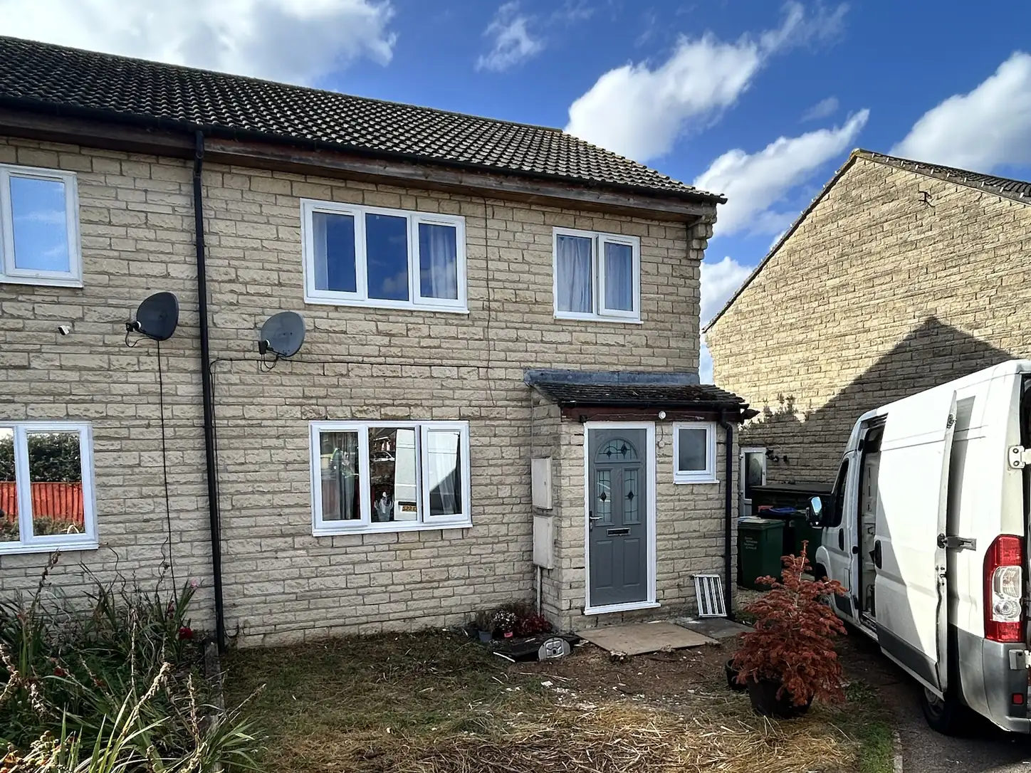 Semi-detached stone-faced house in Cricklade with new white uPVC casement windows and a Shadow Grey composite front door under the porch