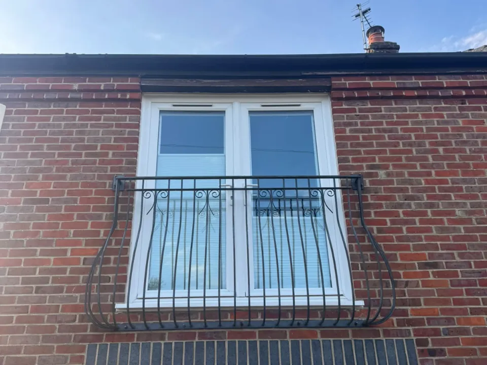 Before: white French doors behind a black Juliet balcony on a red brick house, Sandford-on-Thames